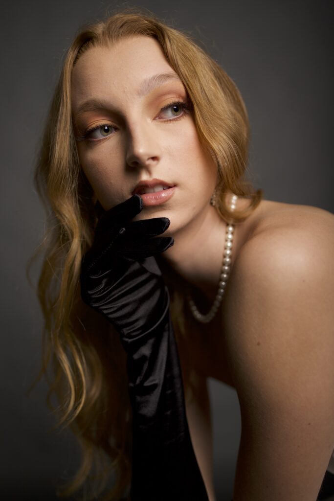 unedited picture of a model, wearing pearls, with one hand on her neck, looking away from the camera