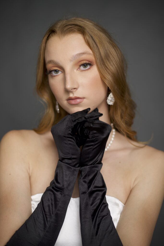 unedited picture of a model wearing pearls, posing with her hands under her chin.